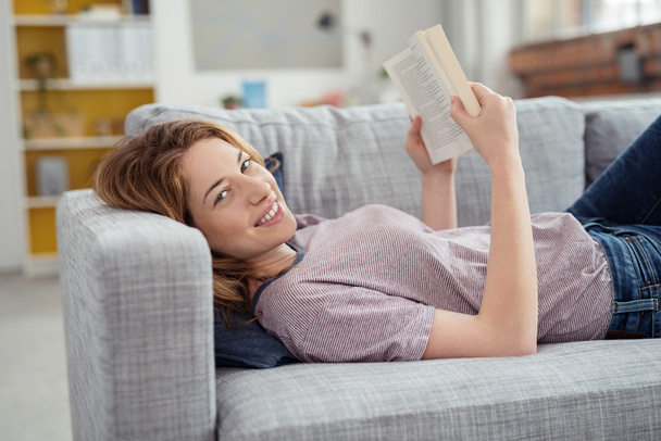 Portrait of Young Woman Lying on Sofa Holding Book - Foto, imagen