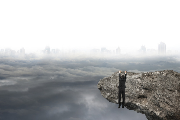 man hand hanging on cliff with gray cloudy sky cityscape - Photo, Image