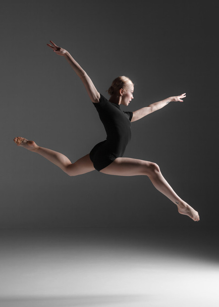 Young beautiful modern style dancer jumping on a studio background - Foto, Imagen