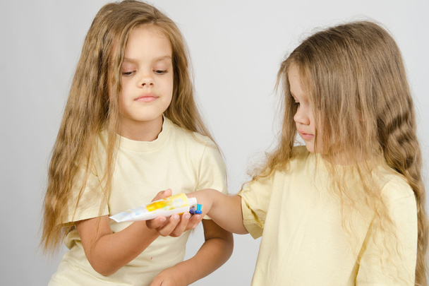 Menina espremendo pasta de dentes de uma irmã tubo
 - Foto, Imagem