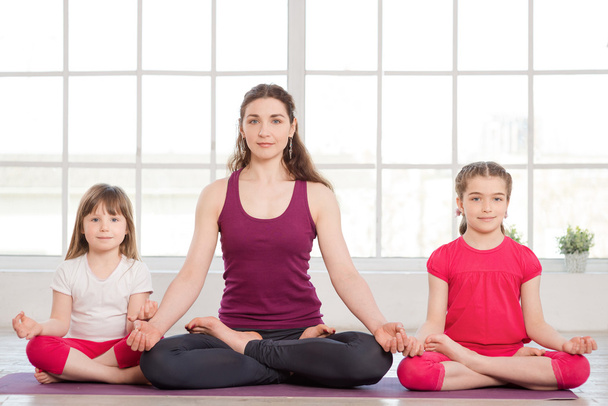 Young mother and daughters doing yoga exercise - Фото, изображение