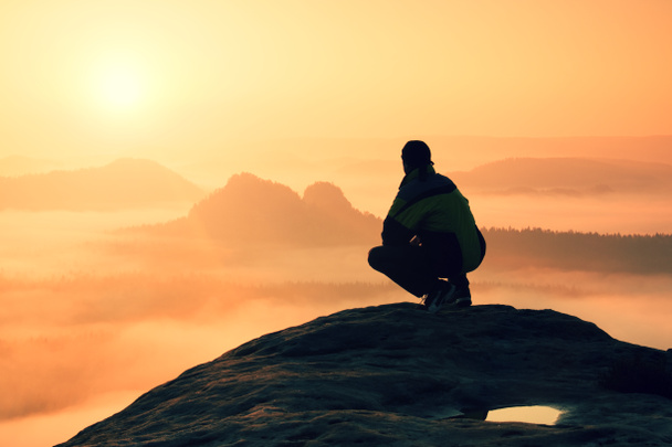 Visão traseira do caminhante masculino sentado no pico rochoso enquanto desfruta de um amanhecer colorido acima do vale das montanhas
 - Foto, Imagem