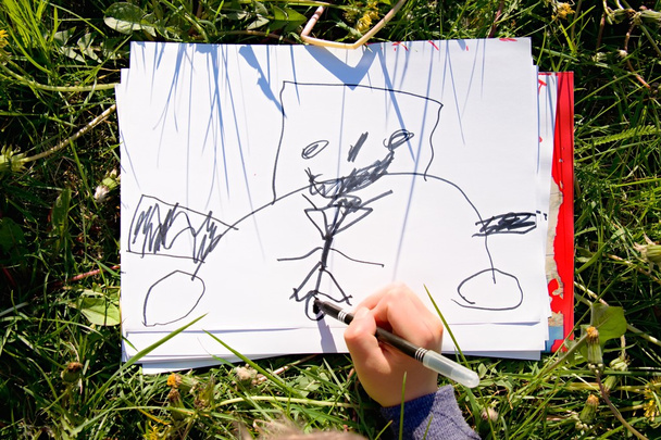 Закройте обзор ручной работы ребенка, рисуя красочные орнаменты на бумаге. Ноутбук в свежей зеленой траве луга
. - Фото, изображение