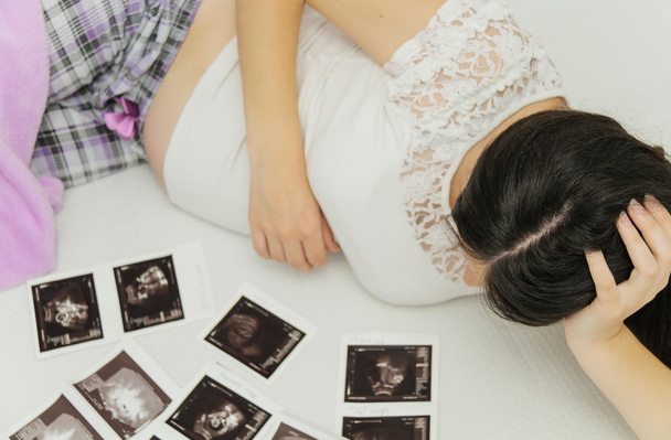 těhotná žena si při pohledu na ultrazvukové vyšetření dítěte - Fotografie, Obrázek