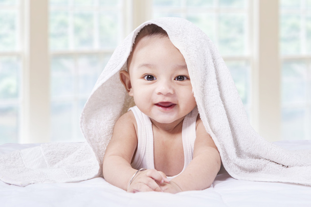 Excited baby boy under towel on bed - Foto, afbeelding