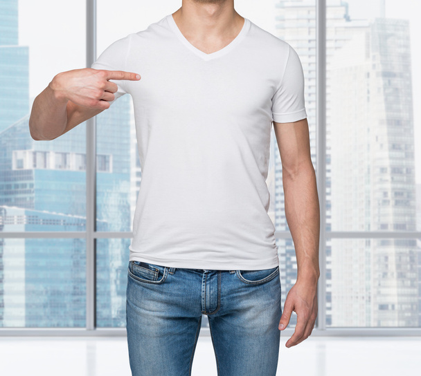 Close-up of a man pointing his finger on a blank t-shirt. New York panoramic view in a modern office. - Foto, Imagen