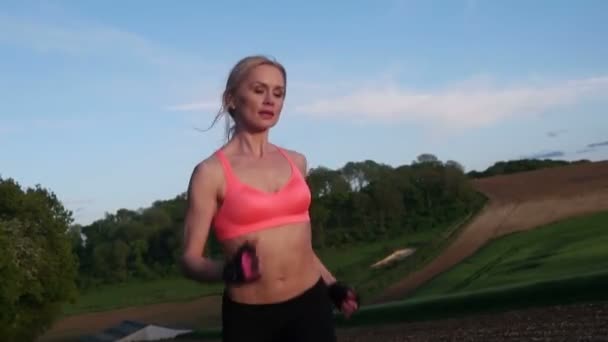 bonita mulher loira correndo e se exercitando no campo durante o pôr do sol
 - Filmagem, Vídeo