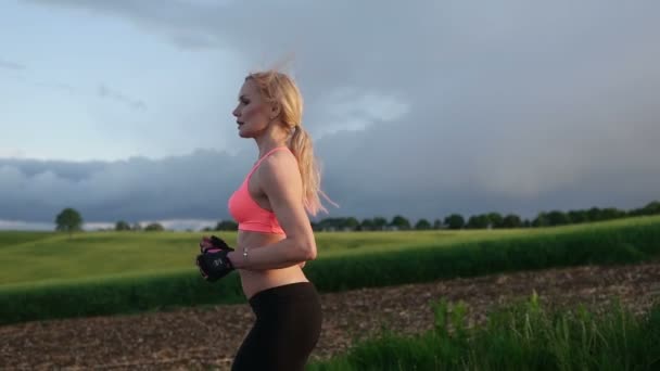 όμορφη ξανθιά γυναίκα τρέχει και την άσκηση στο γήπεδο κατά τη διάρκεια του ηλιοβασιλέματος - Πλάνα, βίντεο