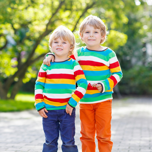 Два маленьких мальчика в разноцветной одежде идут рука об руку
 - Фото, изображение