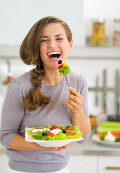 Boldog, fiatal nő, görög saláta eszik a konyhában - Fotó, kép