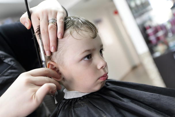 Barber cutting hair of a serious boy - Photo, Image