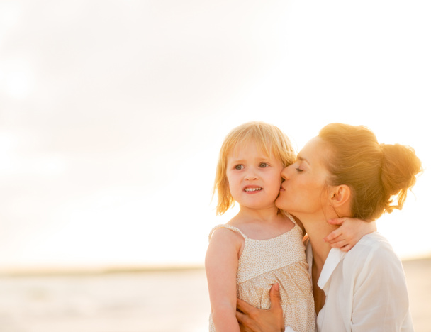 Mother kissing baby girl on beach at the evening - Photo, Image