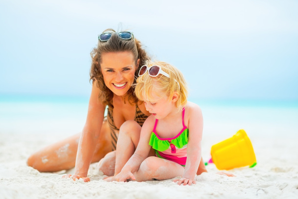 Smiling mother and baby girl playing on beach - Photo, image