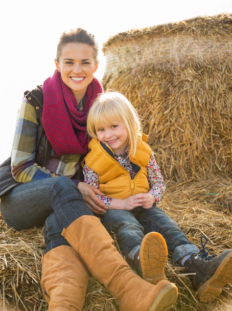 Portrait of happy mother and child sitting on haystack - Foto, imagen