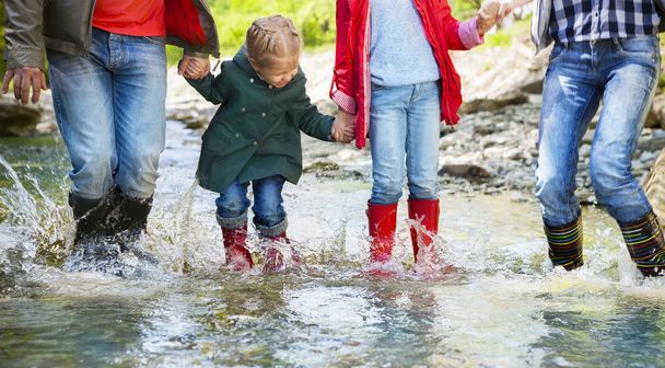 šťastná rodina nošení déšť boty, skákání do horské řeky - Fotografie, Obrázek