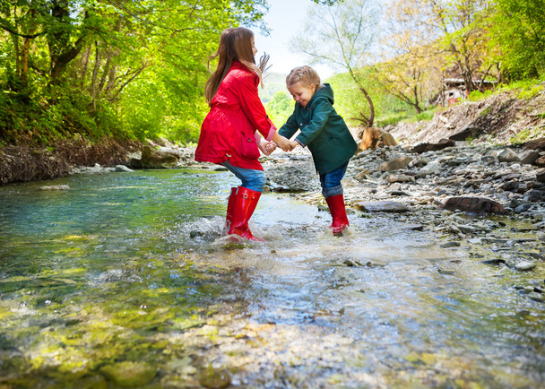 τα παιδιά που φορούν μπότες βροχή άλματα σε ένα ποτάμι βουνό - Φωτογραφία, εικόνα