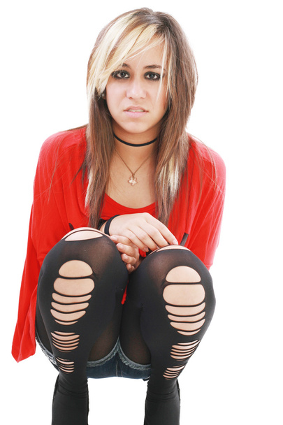 Молодая женщина в панк-одежде наклоняется, чтобы обнять ноги, пока смотрит
 - Фото, изображение