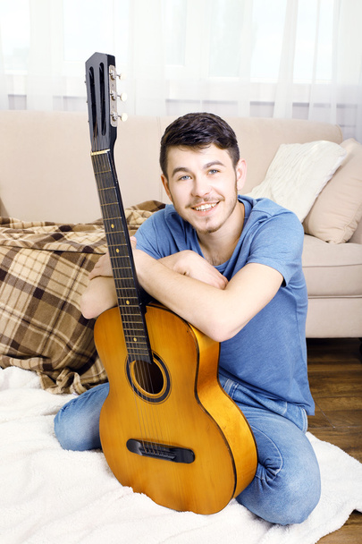 Young man with guitar on floor in room - Фото, изображение