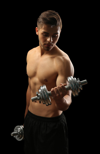 Muscle young man holding dumbbells on dark background - Foto, imagen