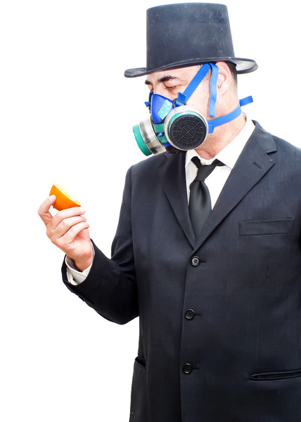 επιχειρηματίας με μάσκα αερίων και καπέλο κοιτάζοντας ένα πορτοκάλι - Φωτογραφία, εικόνα