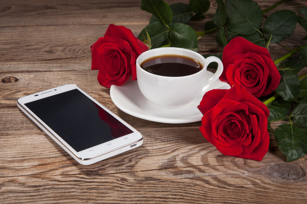 Smartphone, a cup and roses on old table - Photo, image