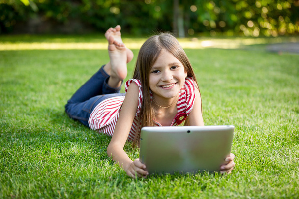 brunette girl relaxing on grass park and holding digital tablet - 写真・画像