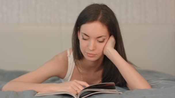 The girl reads the magazine lying on a bed. - Záběry, video
