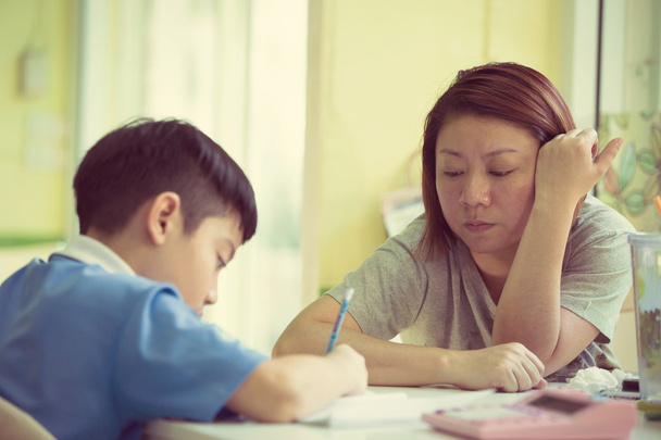 Серьезный азиатская мать помогает сыну с домашней работой
  - Фото, изображение