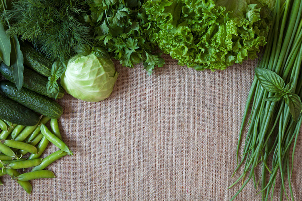 素朴な荒布の背景に緑の野菜のコンポジション フレーム。エンドウ、キャベツ、キュウリ、バジル、ディル、タマネギ, - 写真・画像