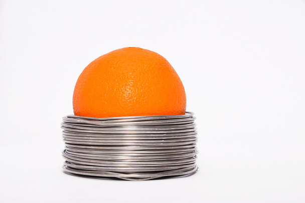Wired orange: whole orange in coils of aluminium wire isolated on white background - Photo, Image