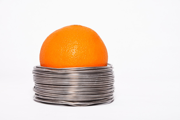 Laranja com fio: laranja inteira em bobinas de fio de alumínio isolado sobre fundo branco
 - Foto, Imagem