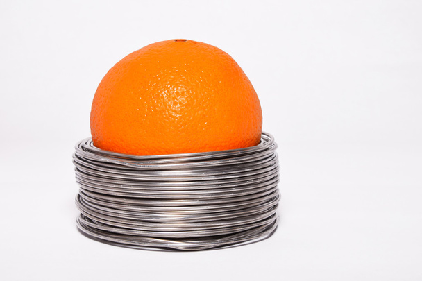 Wired orange: whole orange in coils of aluminium wire isolated on white background - Foto, afbeelding