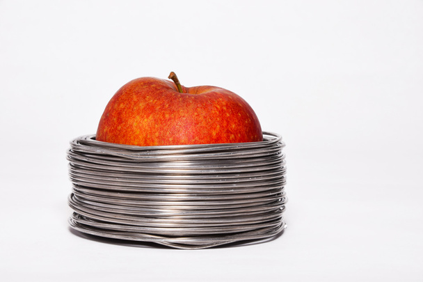 Wired apple: whole red apple in coils of aluminum wire isolated on white background - Foto, afbeelding