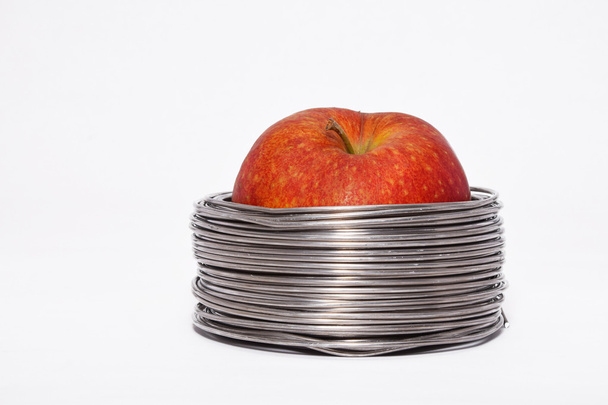 Wired apple: whole red apple in coils of aluminum wire isolated on white background - Φωτογραφία, εικόνα