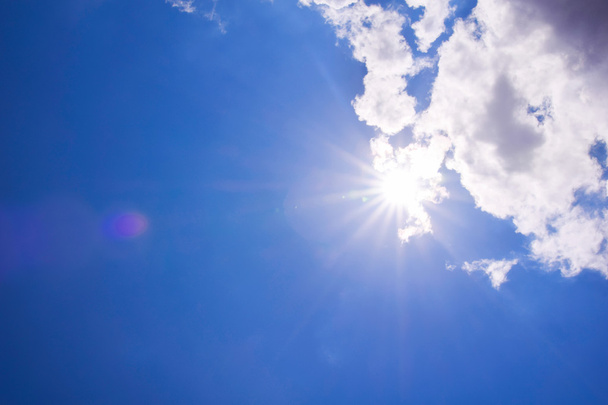 Реалистичное сияющее солнце с бликом объектива. Синее небо с облаками
 - Фото, изображение