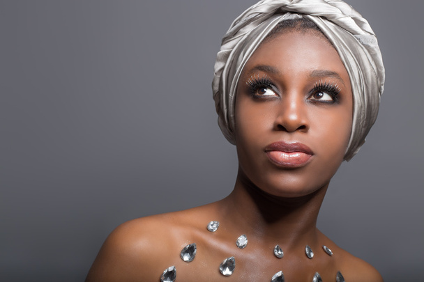 portrait of a beautiful sexy girl with dark black woman in gray kozhoy turban and bright makeup and big full lips with sequins on the body in the studio - Fotografie, Obrázek