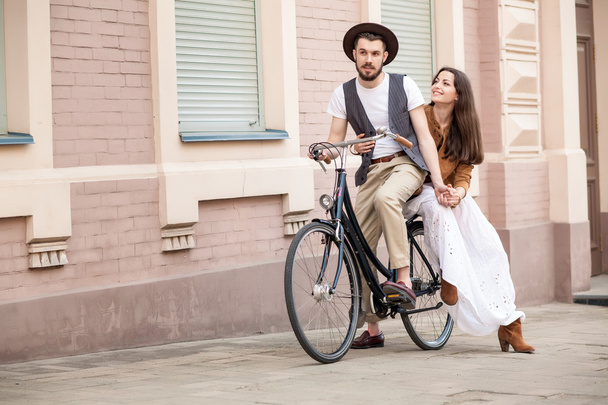 Young couple sitting on a bicycle against the wall  - 写真・画像