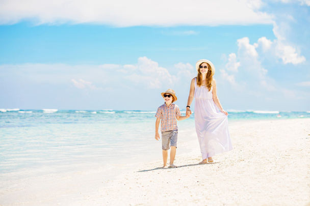 Madre e hijo caminan a lo largo de la playa de arena blanca teniendo grandes vacaciones en familia en la playa de PAndawa, Bali
 - Foto, Imagen