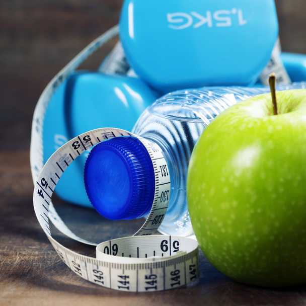 Green apple, dumbbells, water and measuring tape. Health and die - Foto, afbeelding