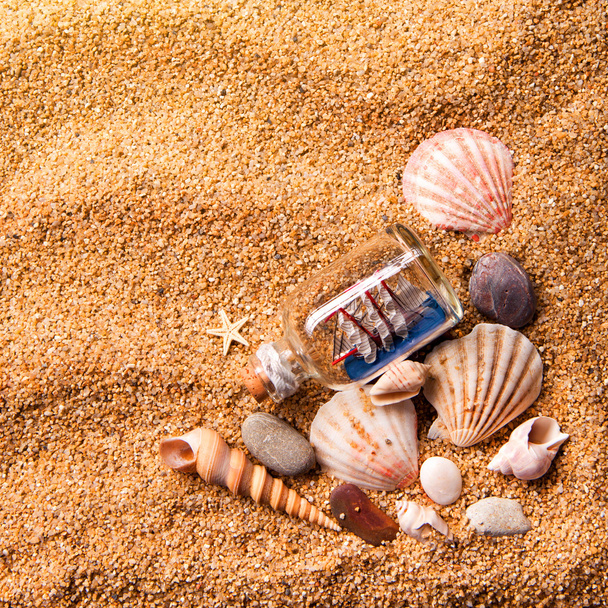 várias conchas e pequeno navio em garrafa na areia
 - Foto, Imagem