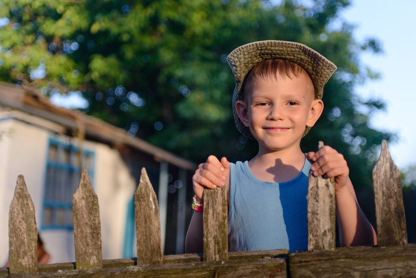 Aranyos fiú: a fából készült kerítés mosolyogva kamera - Fotó, kép