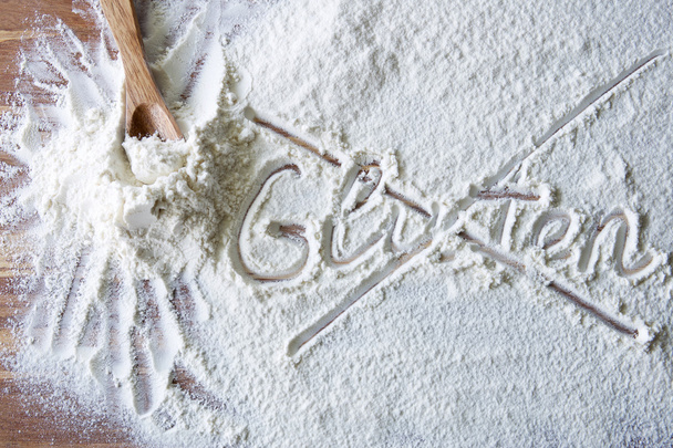 Word gluten crossed out on wood board with flour - Foto, afbeelding
