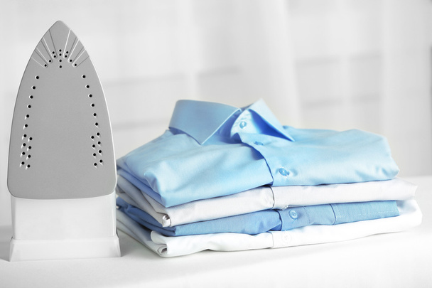 Pile of clothes and electric iron on fabric background - Photo, Image