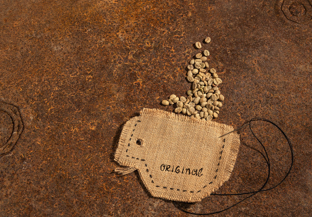 Une tasse cousue en jute avec aiguille et fil plein de grains de café crus placés sur une table rouillée
. - Photo, image