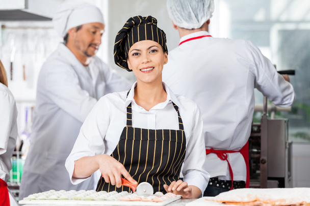 Happy Chef Cutting Ravioli Pasta With Colleagues In Background - Valokuva, kuva