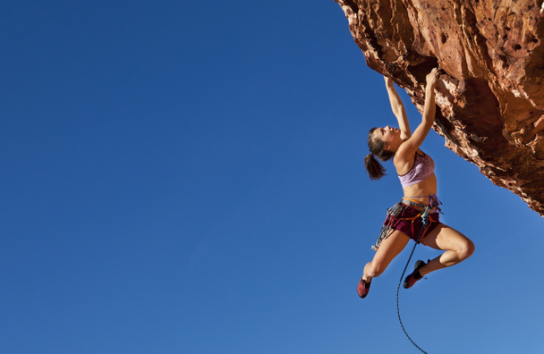 Femme grimpeuse accrochée à une falaise
. - Photo, image