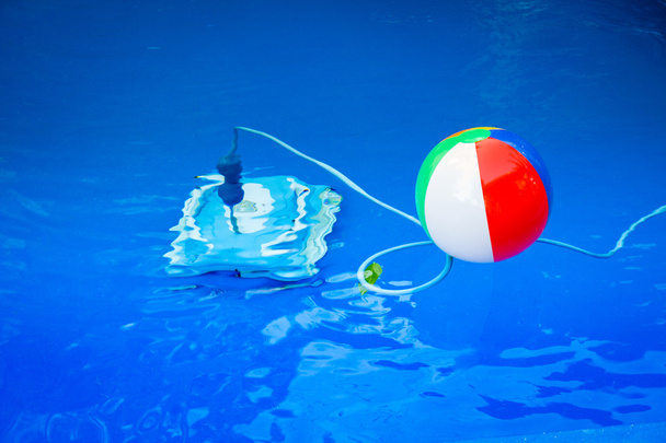 Colorful beach ball floating in pool and next to him underwater a cleaning robot - Foto, afbeelding