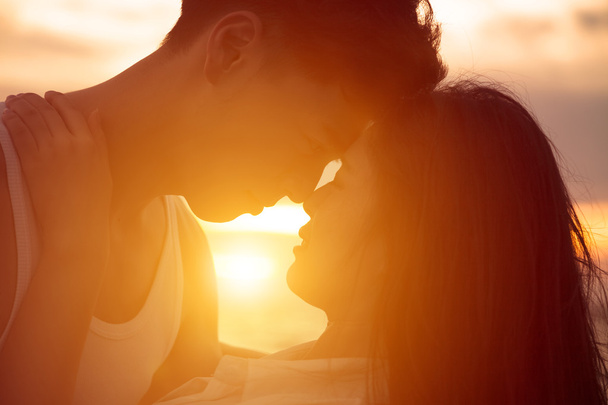 Nuori pari suudella auringonlaskun rannalla
 - Valokuva, kuva