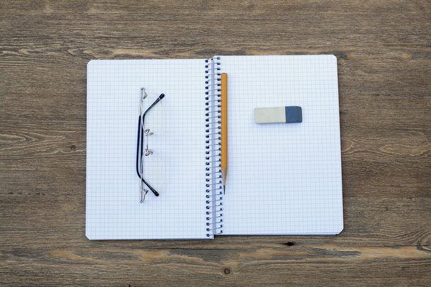 Élargir le bloc-notes en spirale dans une cellule avec un stylo, un crayon, une gomme et des lunettes sur une table en bois, mise au point sélective
 - Photo, image