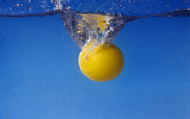 Whole lemon dropped in water against gradient blue background - Photo, image